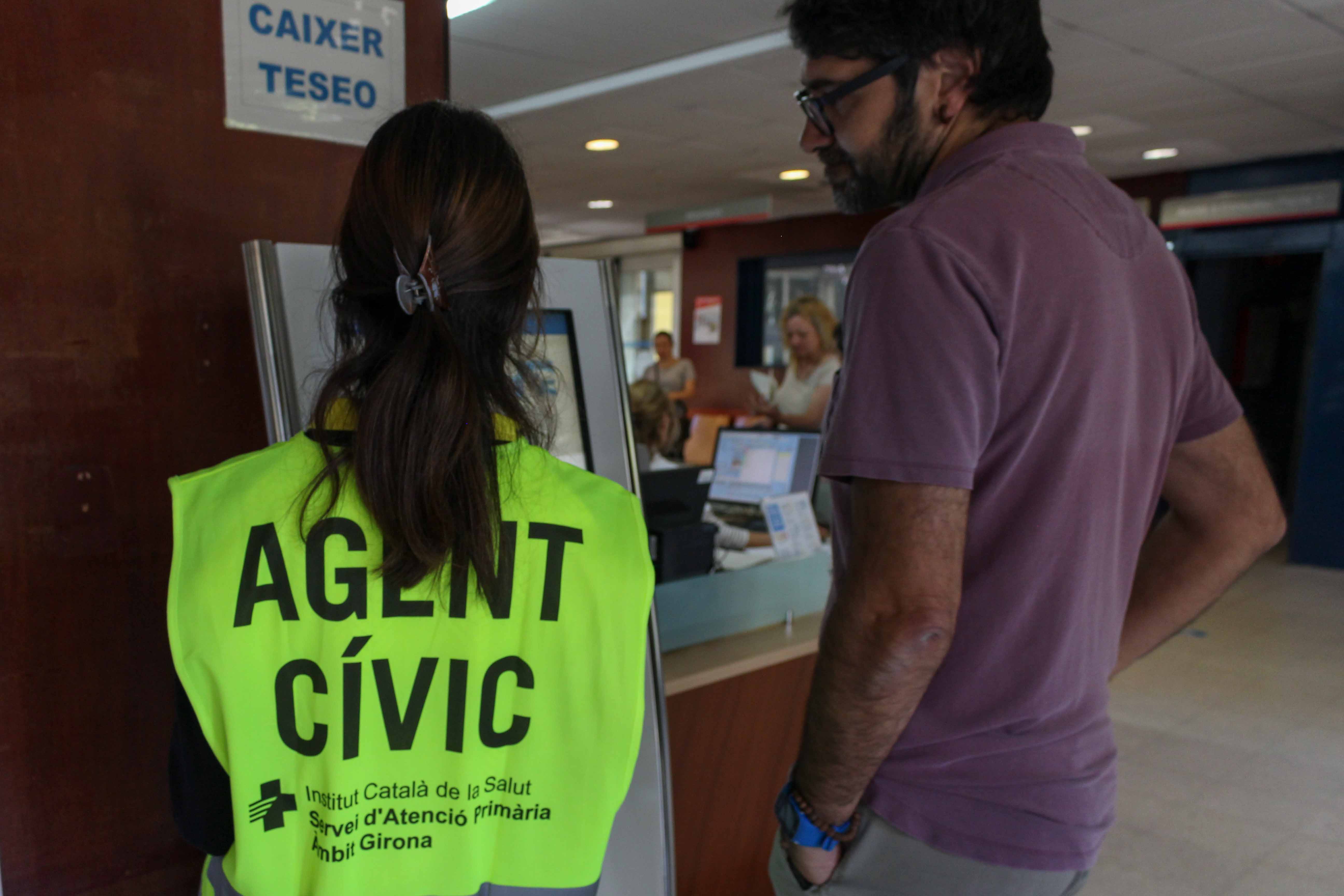 una persona que realitza treballs en benefici de la comunitat ensenya a un usuari el funcionament del caixer TESEO