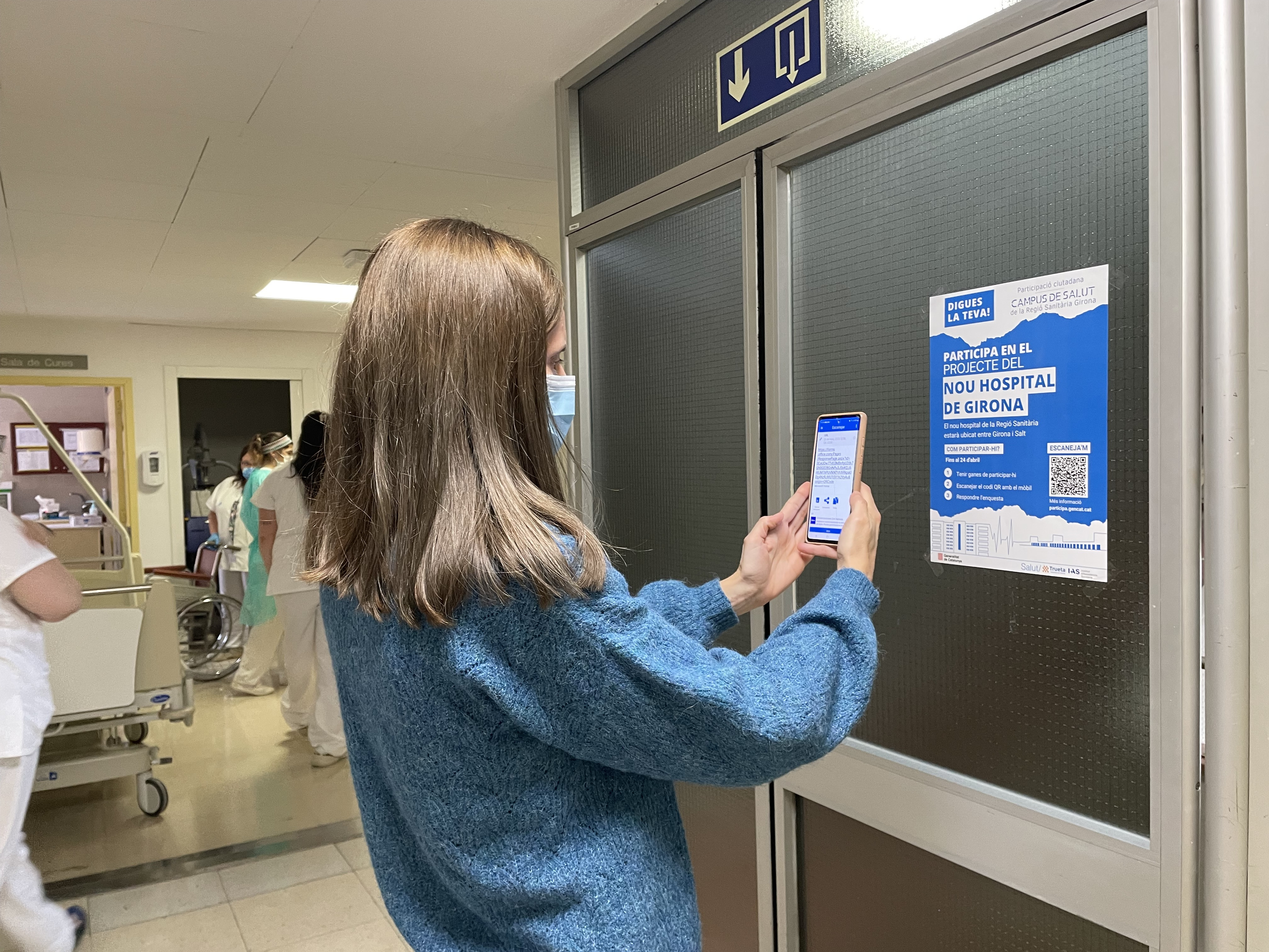 Imatge d'una noia mirant un cartell sobre el procés participatiu per incorporar la veu de la ciutadania en el projecte del nou Campus de Salut de la Regió Sanitària Girona 